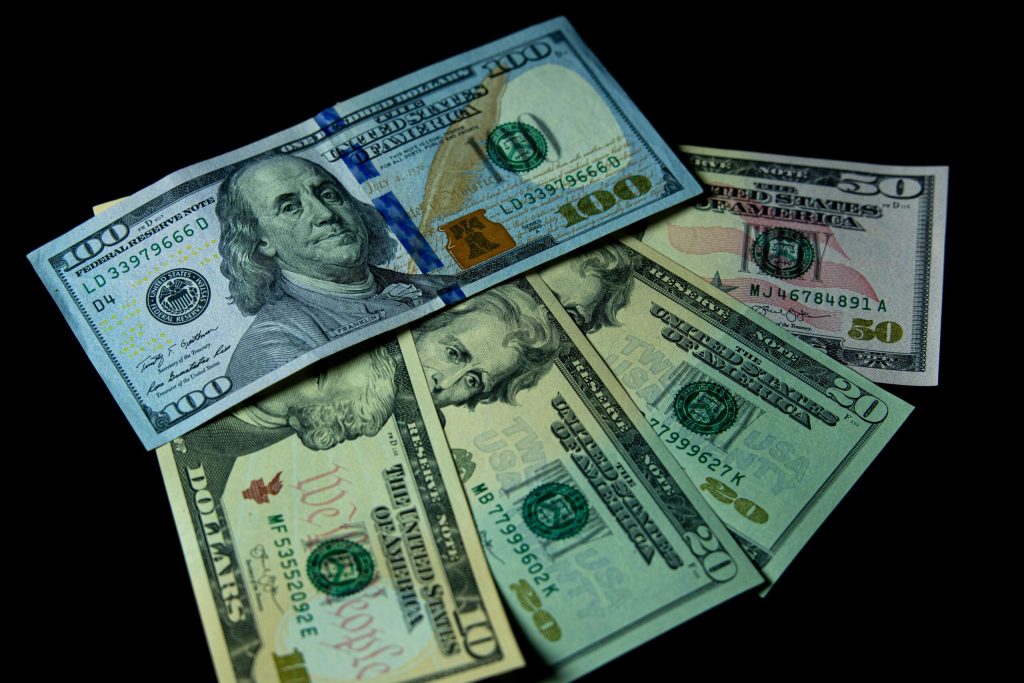 Billetes de dólares y pesos dominicanos junto a productos de consumo que representan el impacto del tipo de cambio en los precios.